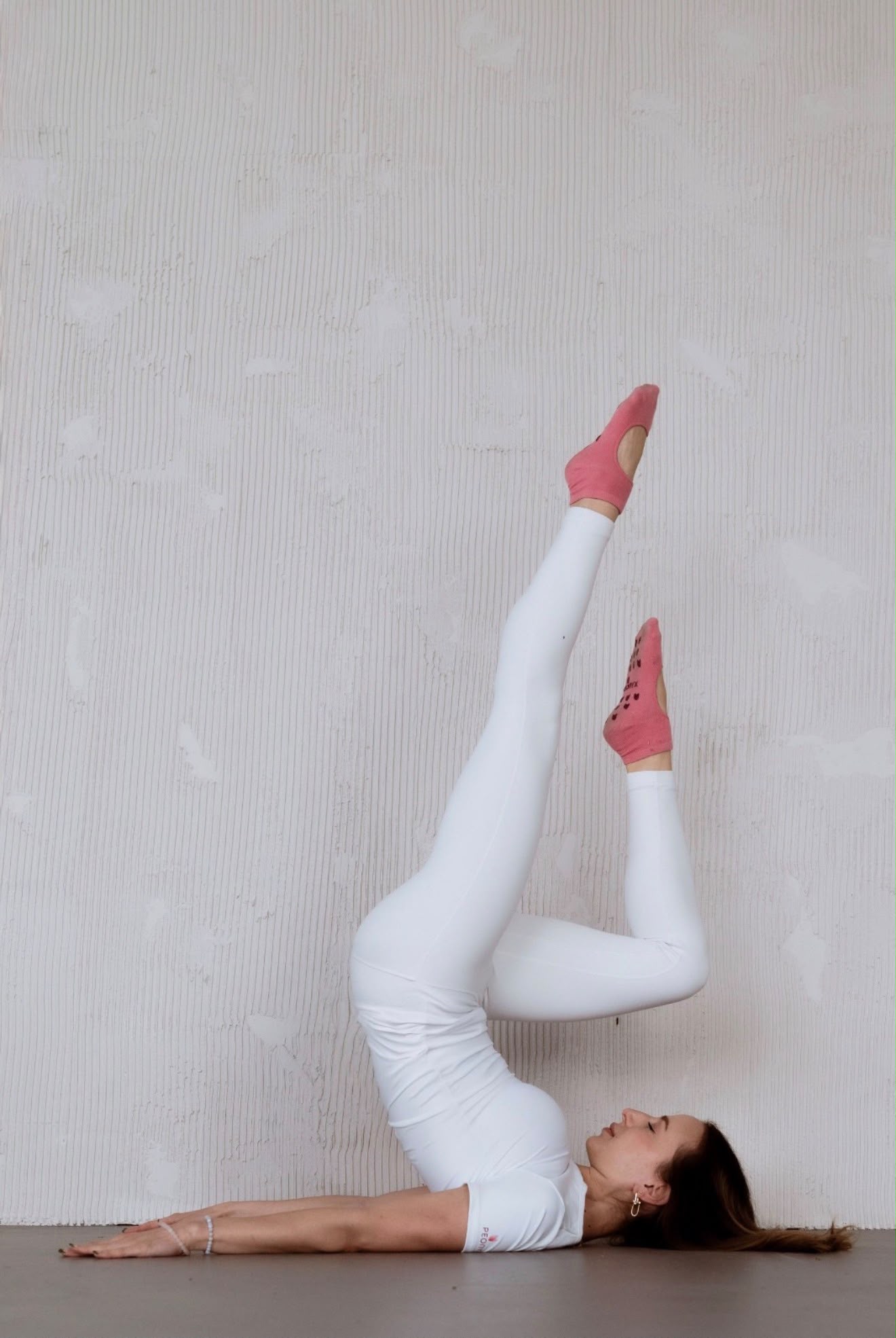 Estie practicing Pilates with her legs extended against a studio wall