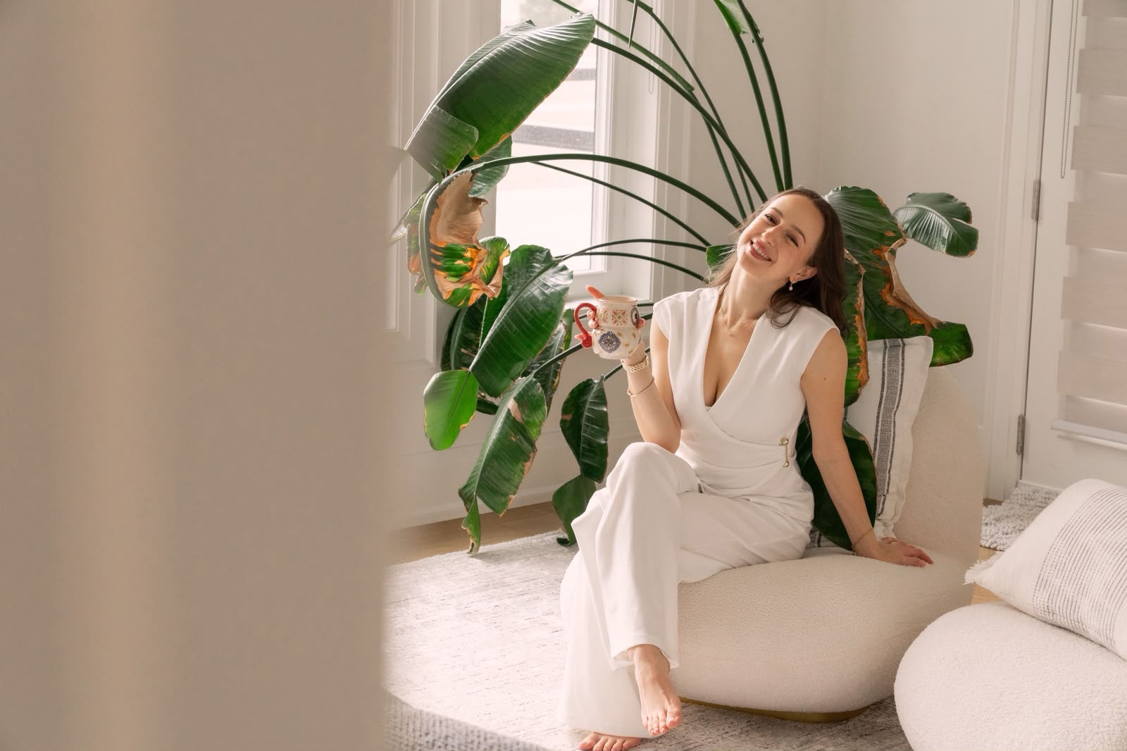 Estie smiling with a cup of herbal tea in a bright room full of plants